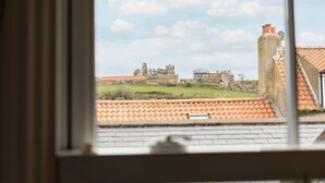 Une vue à travers la fenêtre d’un bâtiment doté d’un toit en tuiles, avec une grande structure historique en arrière-plan.