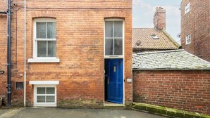 Un bâtiment en briques avec une porte bleue, une petite fenêtre et le numéro « 79 » bien visible sur la porte.