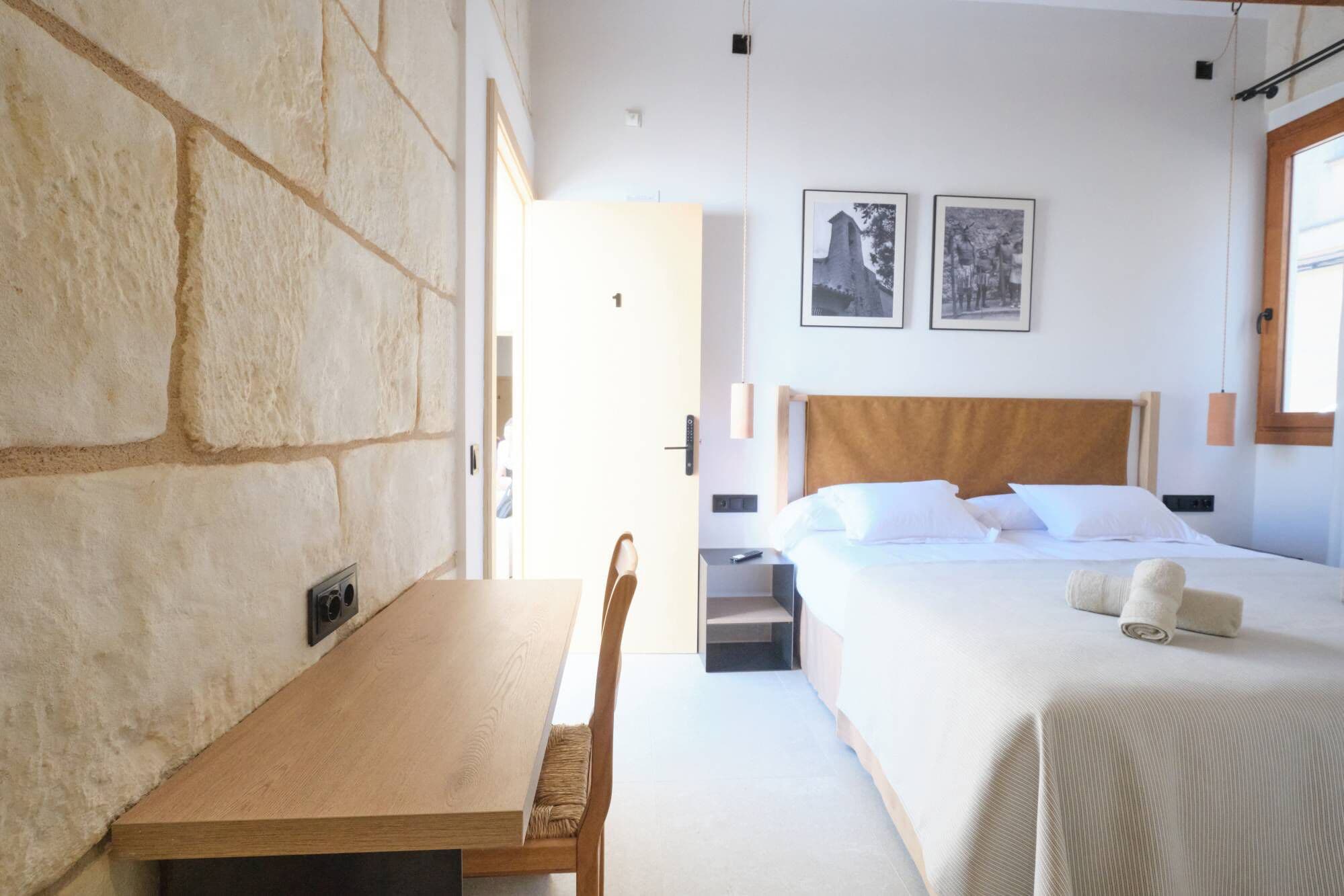 Habitación de hotel moderna con una pared de acento de piedra, un escritorio de madera, una cama con ropa blanca y dos cuadros en la pared.