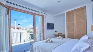 A bedroom with a bed, a TV, a wooden wardrobe, and a balcony with a view of buildings. - Hotel Ca Sa Pagesa (Santa Margalida)