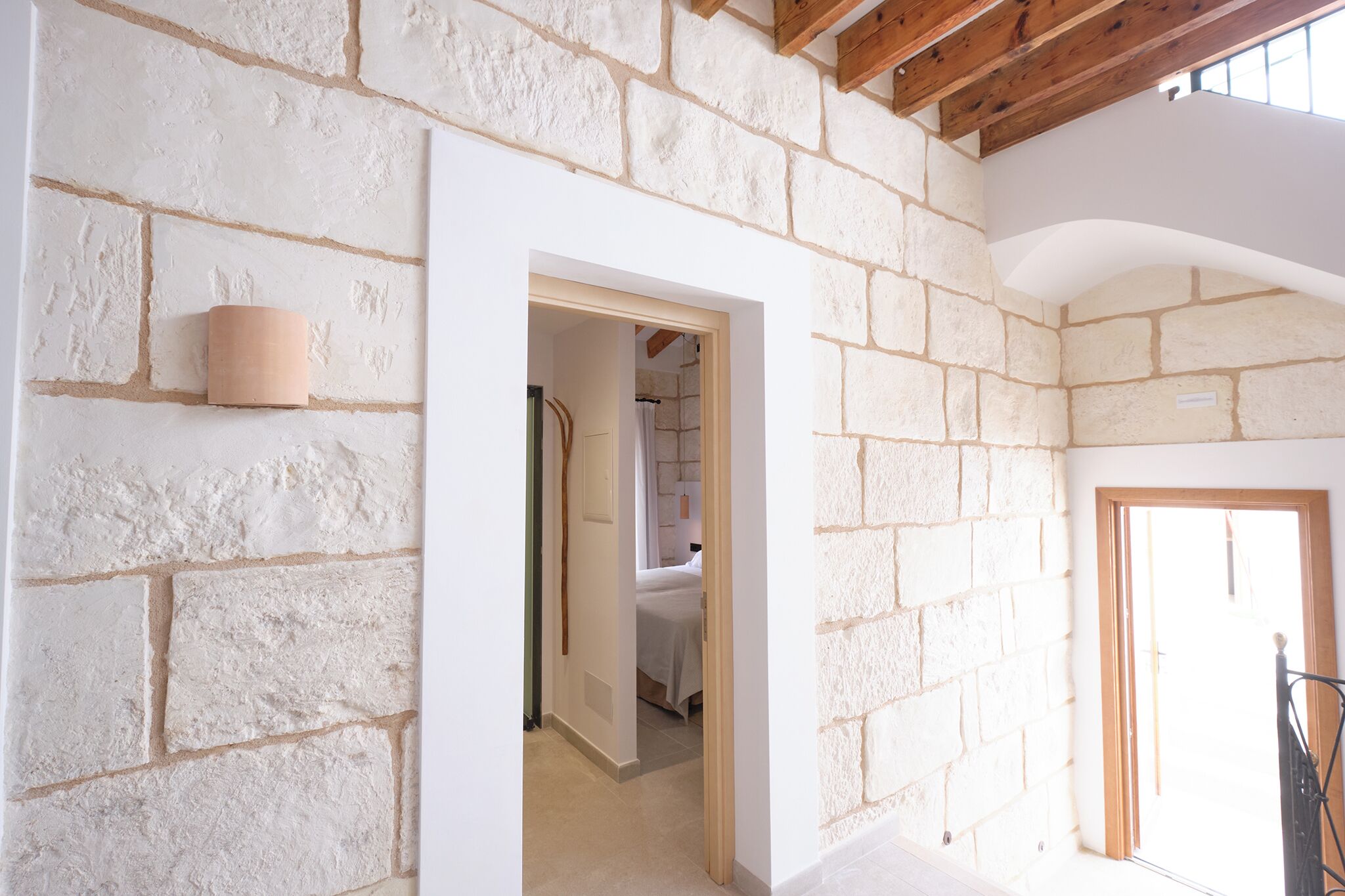 Una habitació amb parets de pedra vista, un biga de fusta al sostre i una porta que condueix a una altra estança.