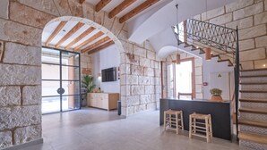 A spacious kitchen with stone walls, wooden beams, and a modern island with stools. - Hotel Ca Sa Pagesa (Santa Margalida)