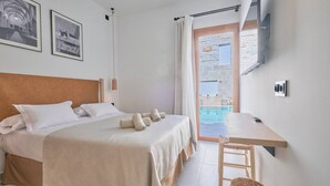 A bedroom with a bed, a wooden headboard, a bedside table, a TV mounted on the wall, and a view of a swimming pool through a glass door. - Hotel Ca Sa Pagesa (Santa Margalida)