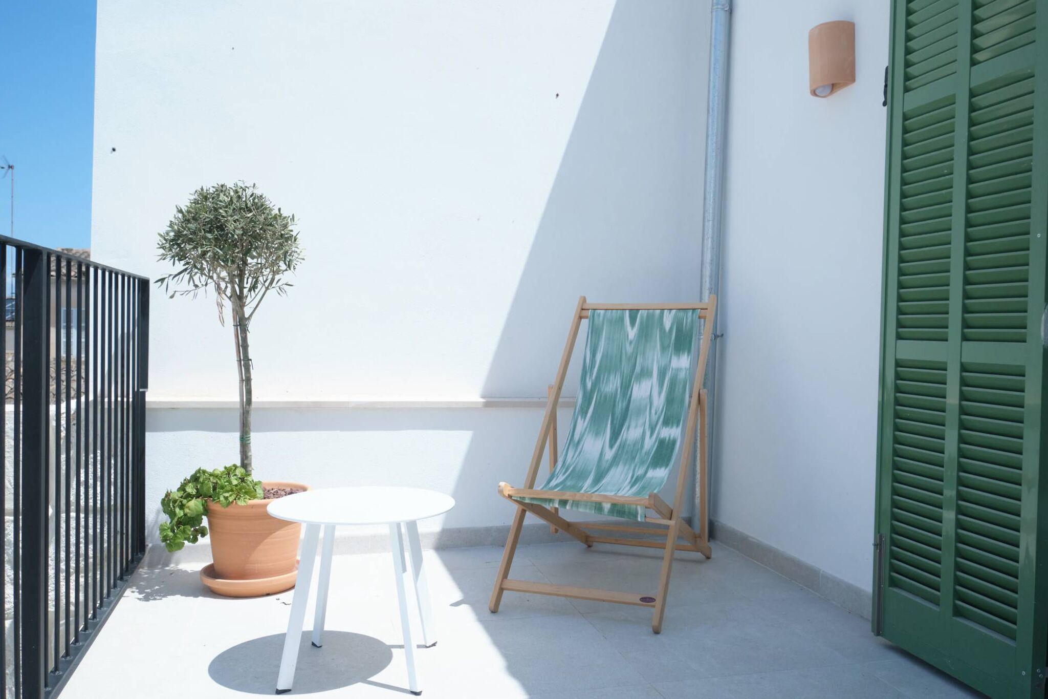 Un balcon avec un pot de fleurs, une petite table et un chevalet.