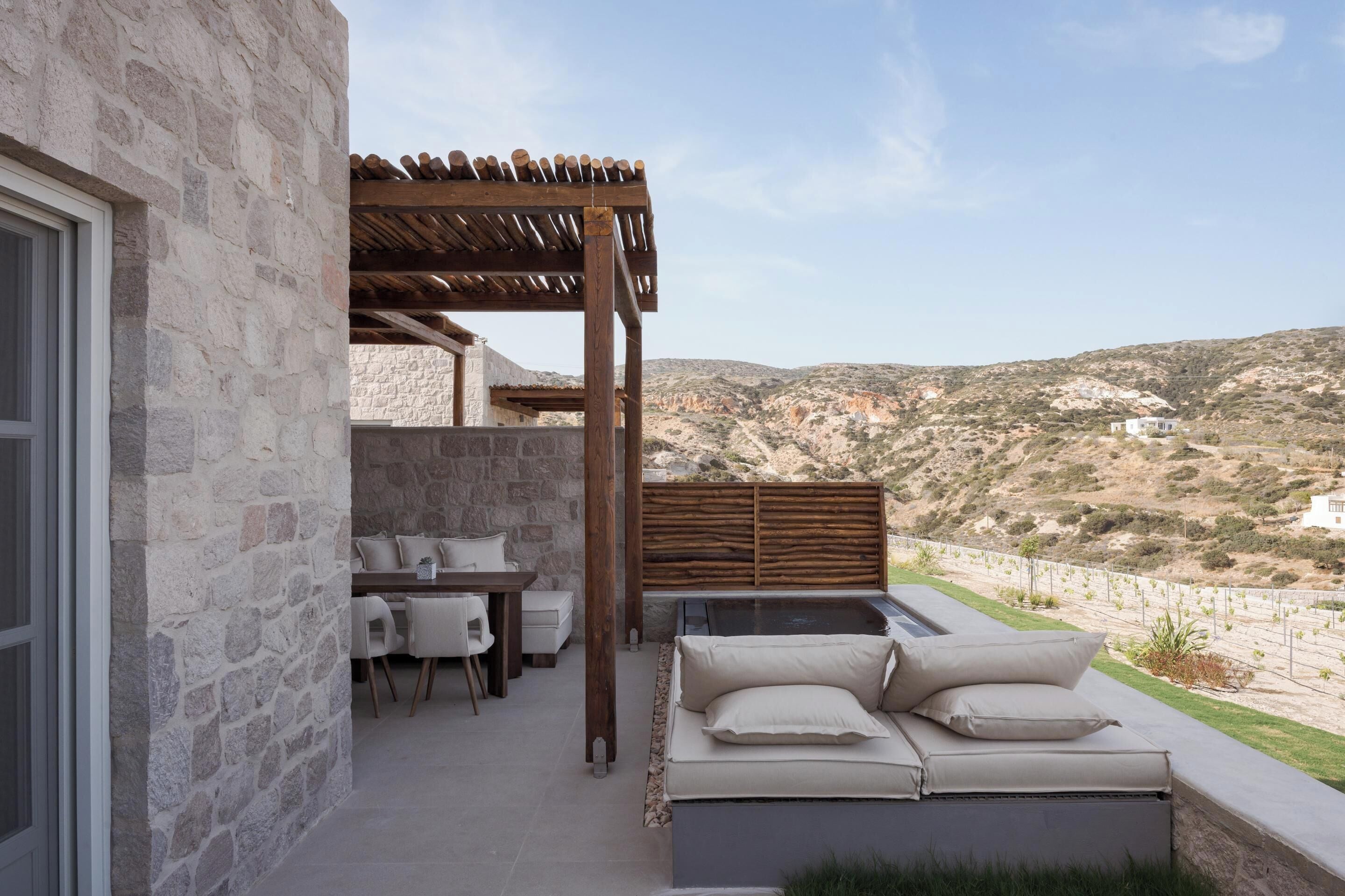Un edificio in pietra con un patio che include una pergola in legno, posti a sedere all'aperto e vista su un paesaggio collinare.
