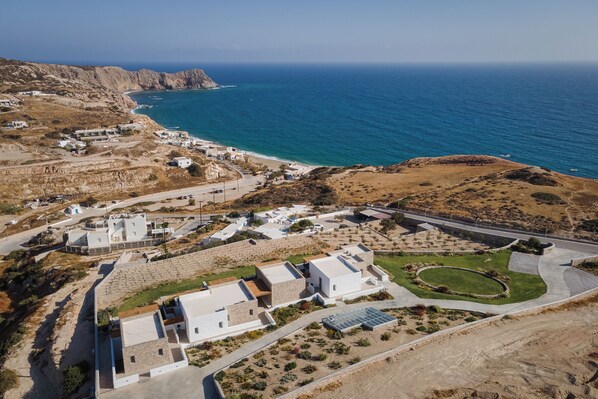 An aerial view of a coastal residential area with houses, a road, and a beach. - Horizon Suites Milos (Milos)