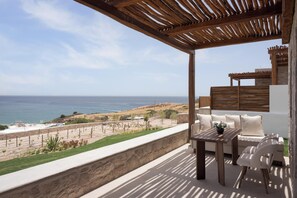A balcony with a wooden pergola, a table, and a sofa overlooking a coastal landscape. - Horizon Suites Milos (Milos)