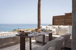 A terrace with a table set for breakfast overlooking the sea, featuring a view of the coastline. - Horizon Suites Milos (Milos)