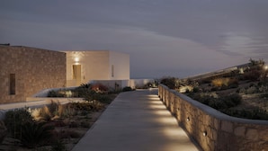 A modern building with a stone facade, a concrete pathway, and a stone retaining wall. - Horizon Suites Milos (Milos)