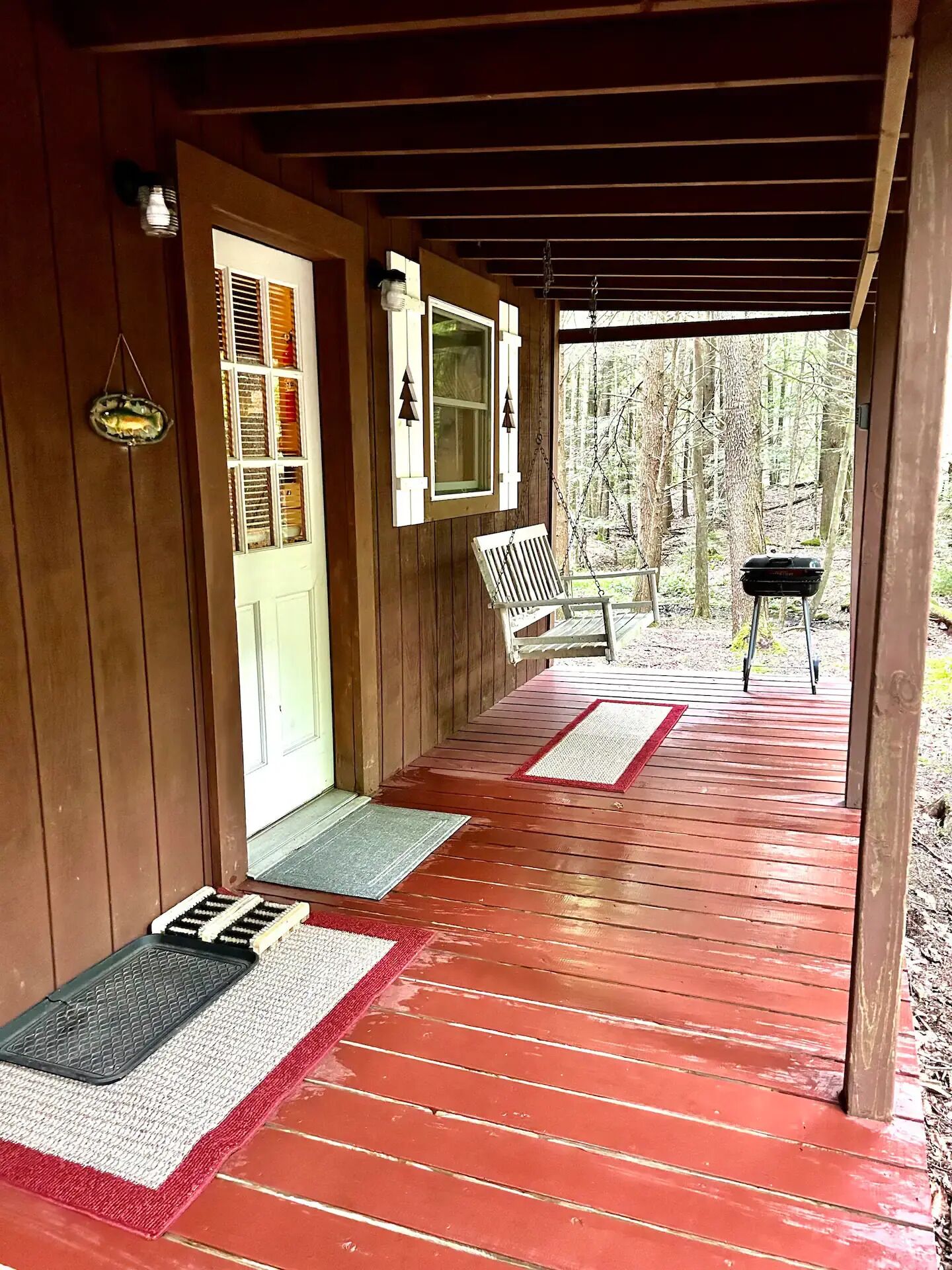 A wooden porch with a bench, a door with shutters, and a view of the forest.