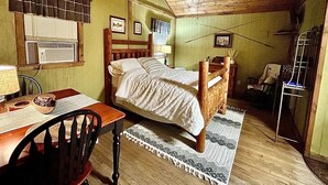 A bedroom with a wooden ceiling fan, a bed with a wooden headboard, a desk with a chair, and a window with blinds. - Glady Hideaway (Bowden)