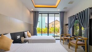Ein Hotelzimmer mit zwei Betten, einem kleinen Tisch und einer Sitzecke an einem Fenster mit Vorhängen.