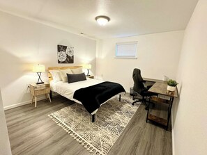 A bedroom with a bed, bedside tables, a desk, a chair, a rug, and a wall-mounted artwork.