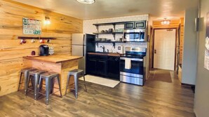 A compact kitchen with a wooden bar area, stainless steel appliances, and a visible door leading to another room.