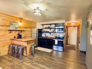 Eine kleine Küche mit einer Holztresen-Bar, Edelstahlgeräten und einer sichtbaren Tür zu einem anderen Raum.