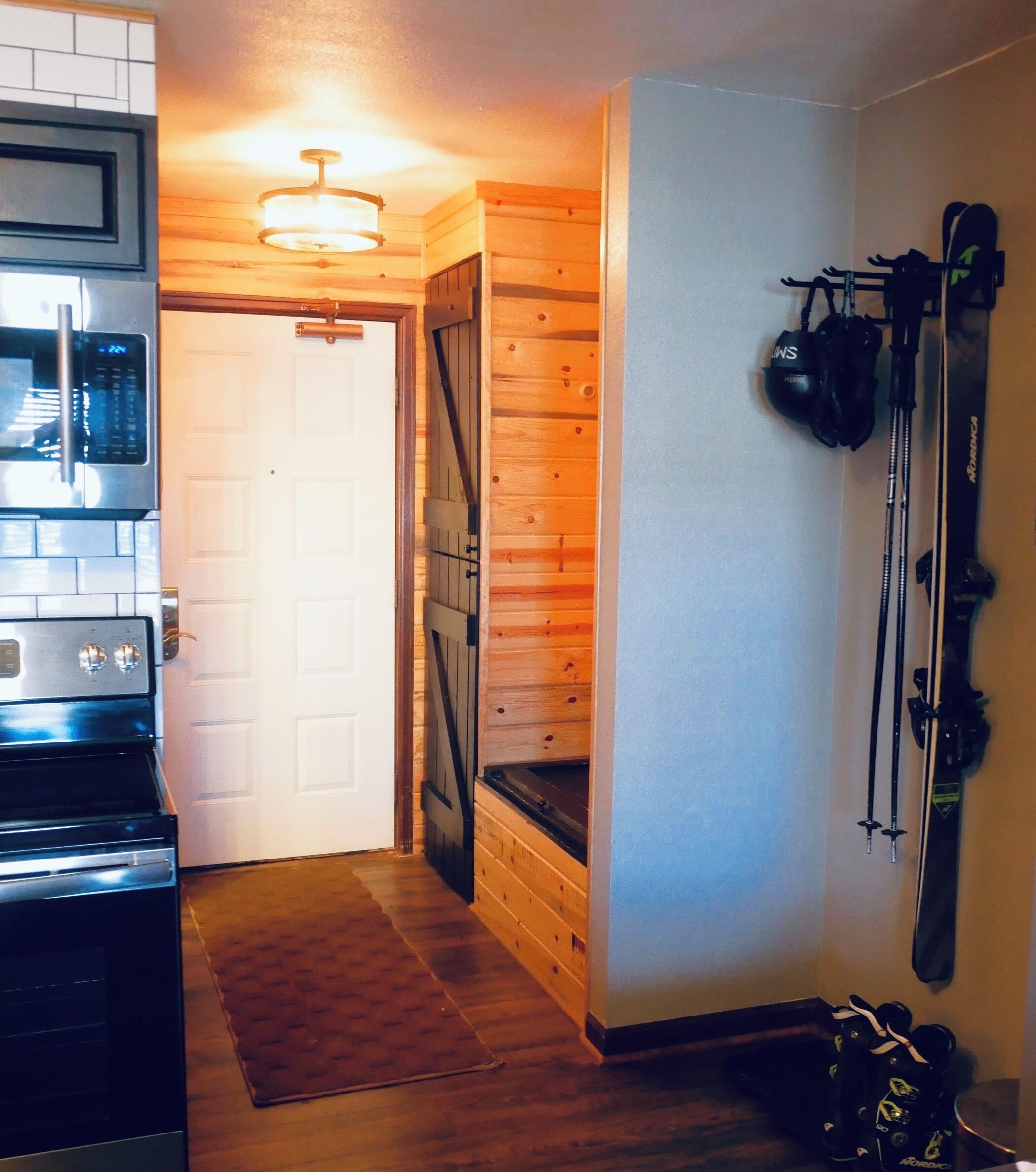 Eine Küche mit Mikrowelle, Backofen und einer Holztür zu einem Raum mit Skiern und Skistöcken.