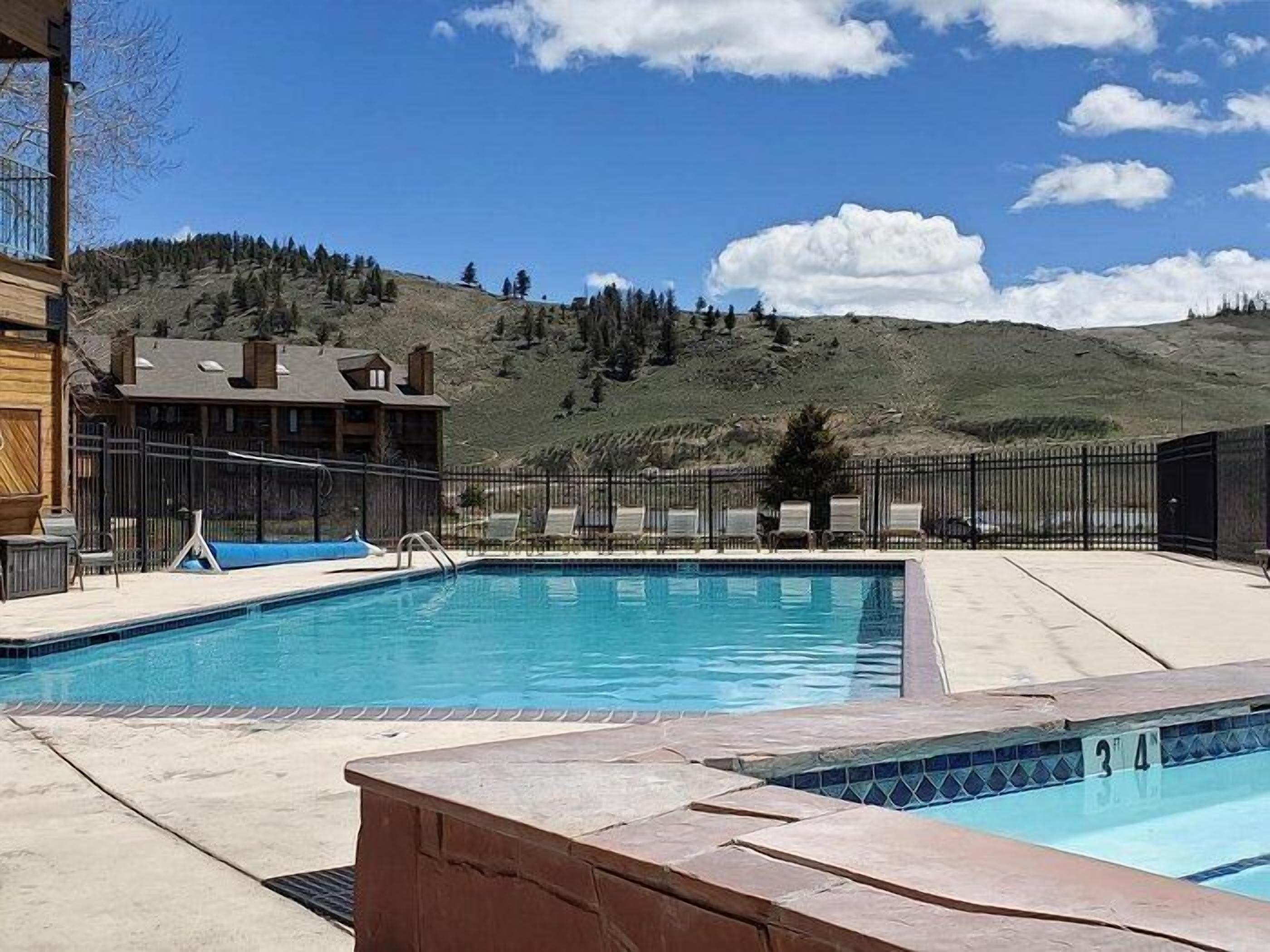 Une piscine avec vue sur une montagne, une zone délimitée par une clôture et un bâtiment en arrière-plan.