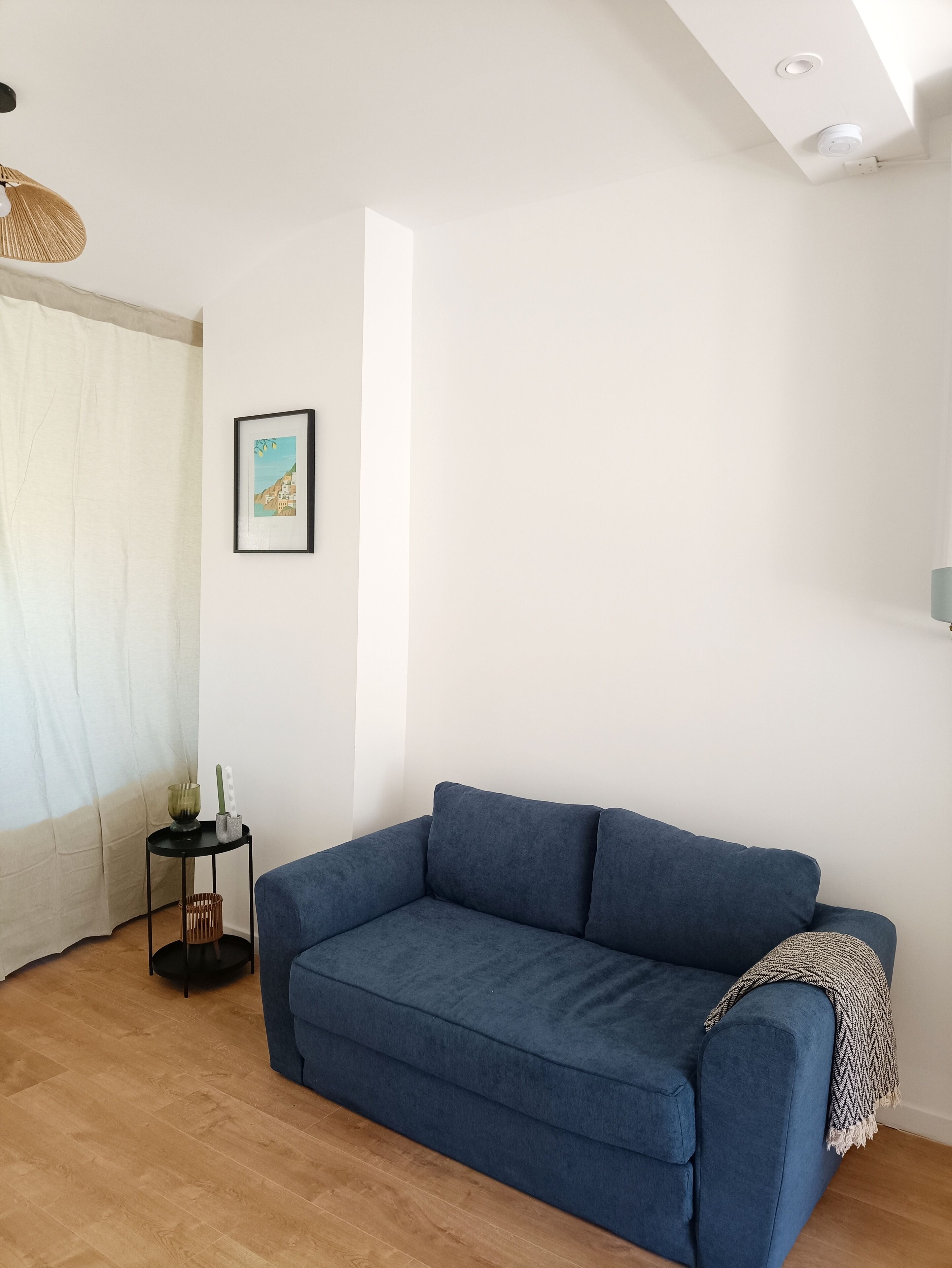 Un salon moderne avec un canapé bleu, une petite table d’appoint, un tableau encadré et un luminaire au plafond.