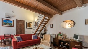 A living room with a red sofa, a beige armchair, a wooden TV stand, and a staircase. - Loft Della Rosa by Wonderful Italy (Palermo)