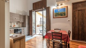 A kitchen with wooden cabinets, a dining table with chairs, and a painting on the wall. - Loft Della Rosa by Wonderful Italy (Palermo)