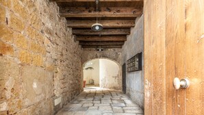 A narrow stone corridor with a wooden door and a hanging light fixture. - Loft Della Rosa by Wonderful Italy (Palermo)