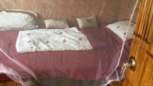 Un dormitorio con cama cubierta por una cortina ligera, cabecera de madera y dos almohadas con texto.