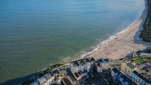 Vista aérea de un pueblo costero con una playa de arena, un puerto deportivo y edificios residenciales con áreas de estacionamiento.