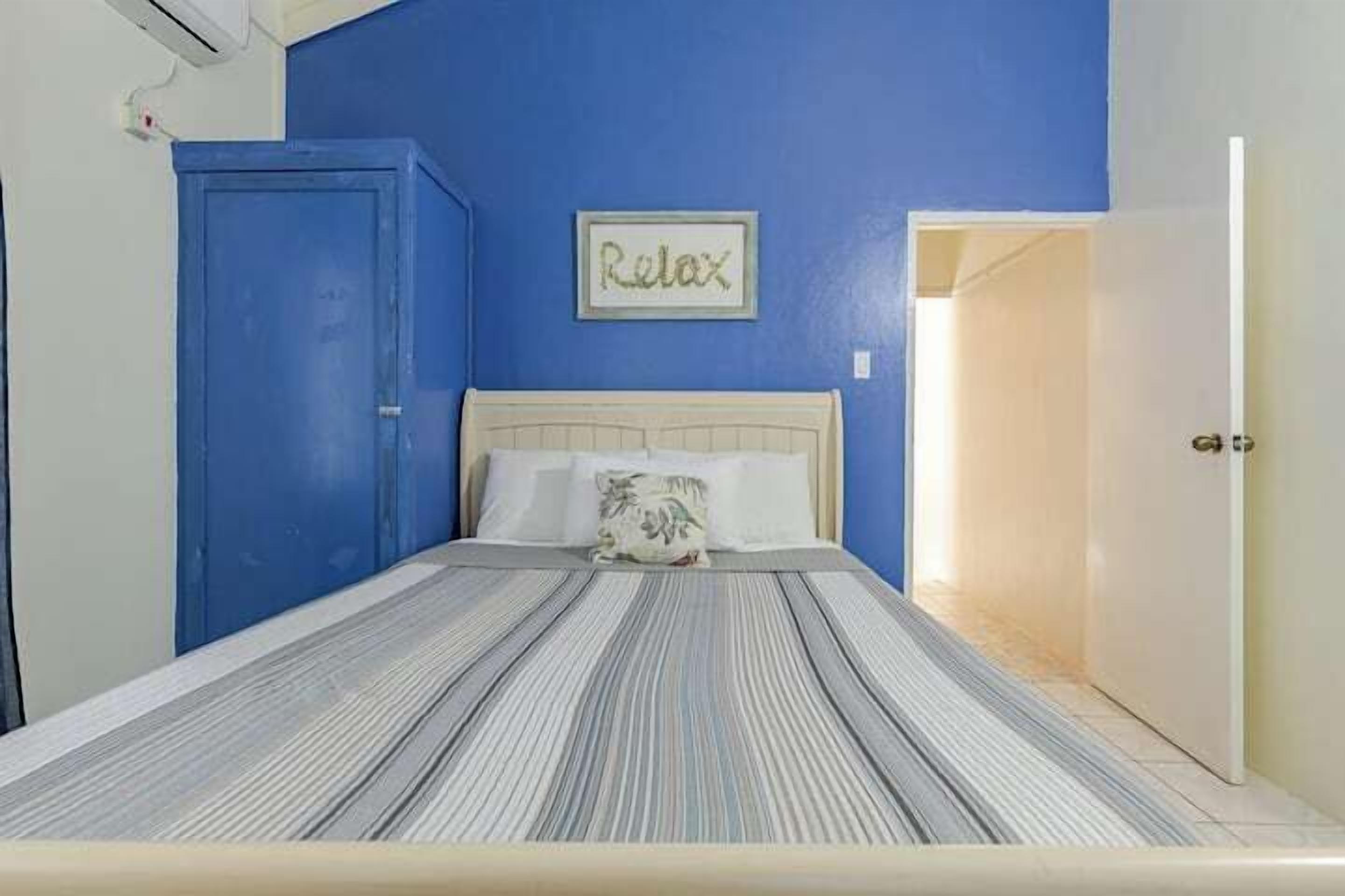 Un dormitorio con cama, pared azul, una puerta y un cartel que dice "Relax".