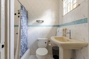 A small bathroom with a toilet, sink, and shower curtain. -  The Dream Nest At Csompo Silver Manor (Tower Isle)