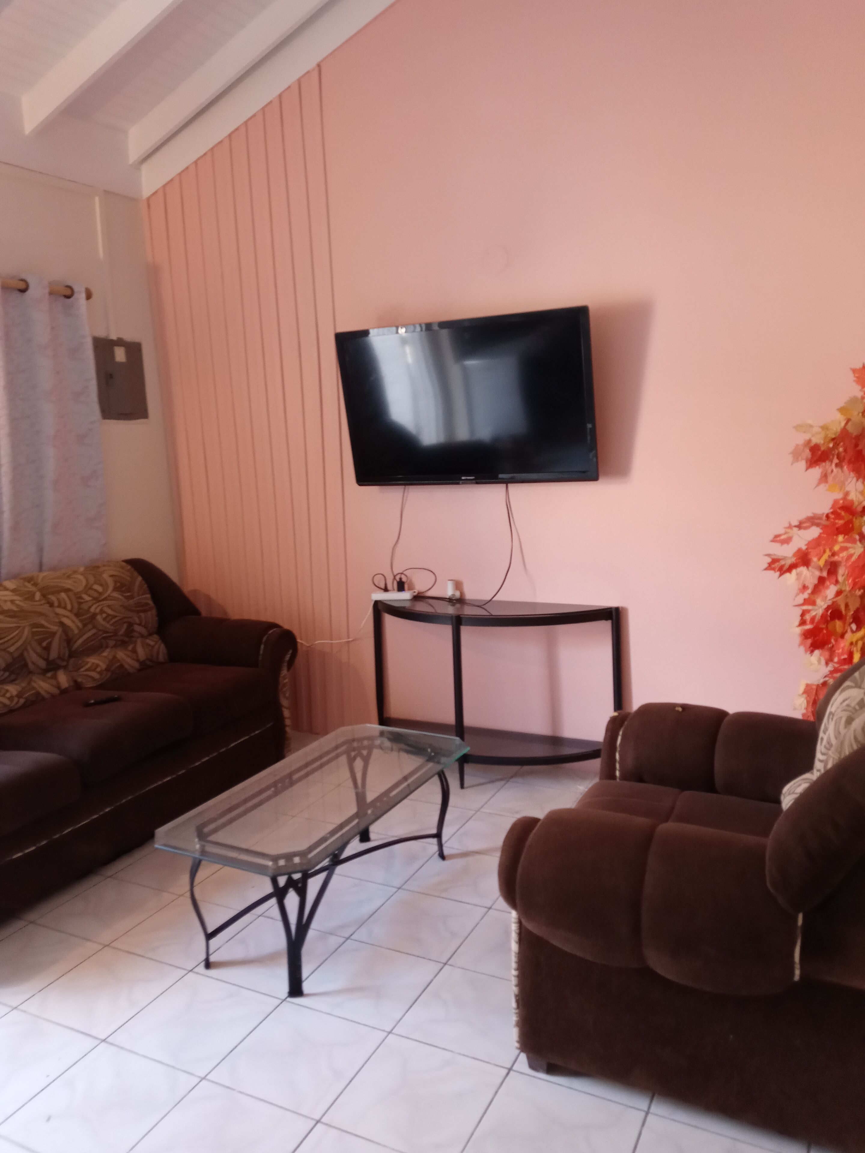 Un salon comprenant un canapé, une table basse, un téléviseur fixé au mur et une petite table avec une lampe.