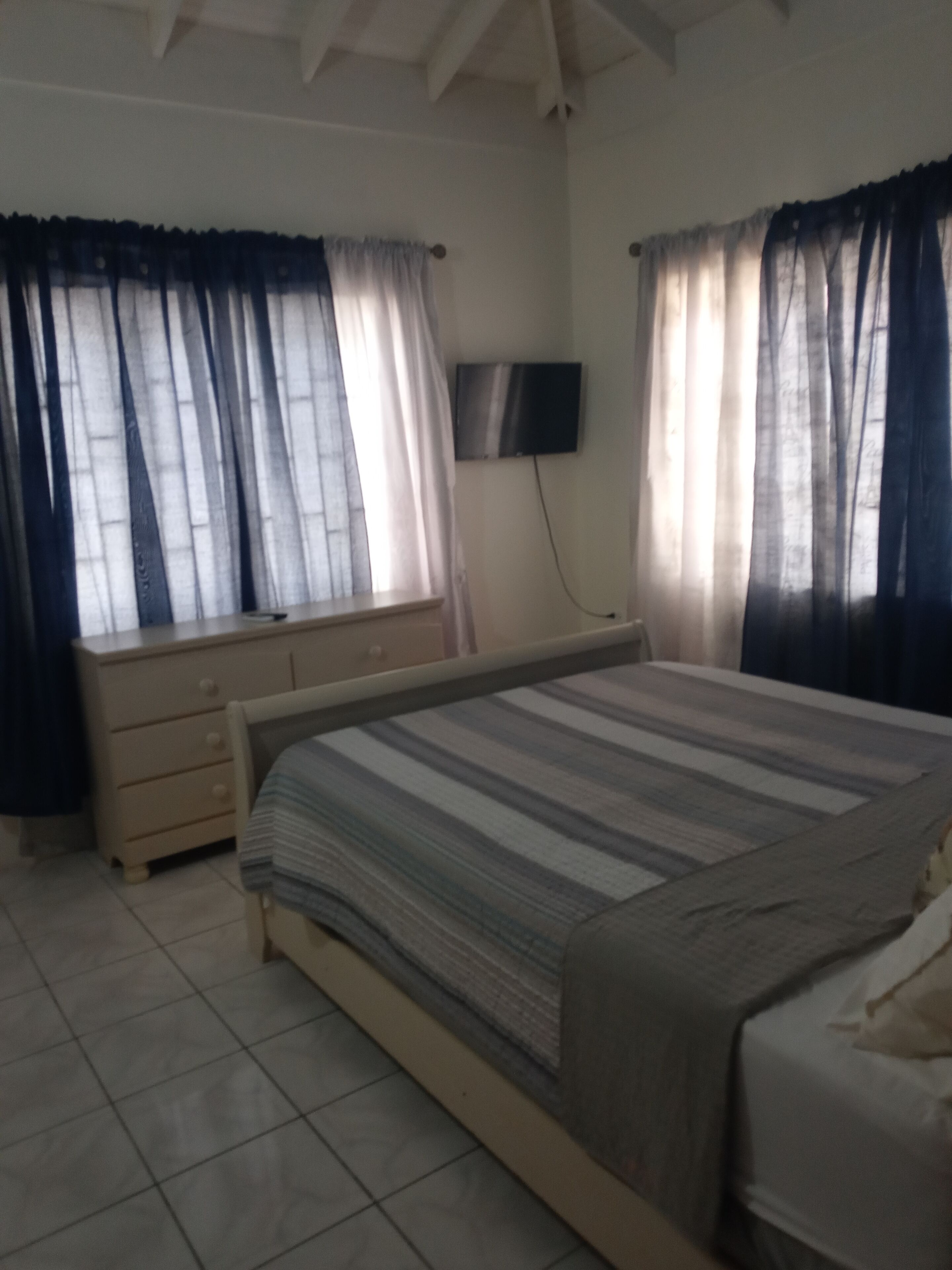 A bedroom with a bed, a TV mounted on the wall, and a window with curtains.