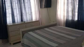 A bedroom with a bed, a TV mounted on the wall, and a window with curtains.