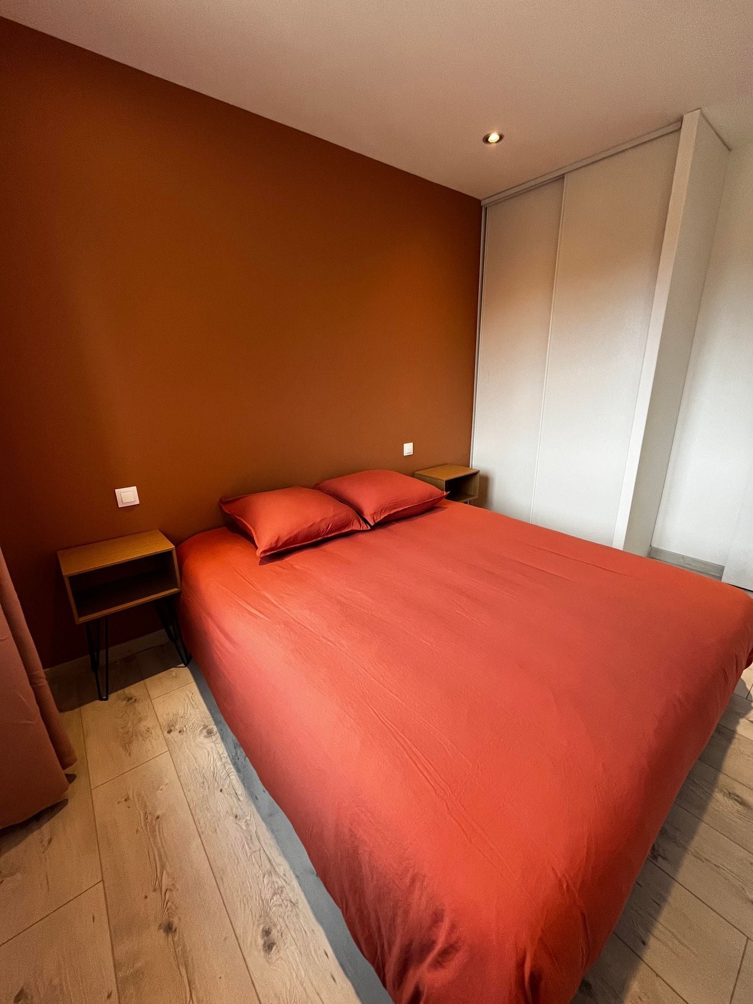 A bedroom with a large bed, wooden flooring, and a nightstand with a lamp.