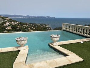 Una piscina con dos macetas decorativas, vista despejada al mar y una cadena montañosa distante.
