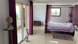 Een slaapkamer met een bed, een beeld, een koffer en uitzicht op het omliggende landschap.