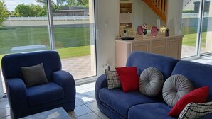A living room with a blue sofa, a blue armchair, and a white cabinet with decorative items. - Gîte L'escale Portsallaise (Ploudalmézeau)