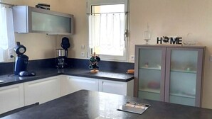 A kitchen with a dark countertop, a coffee maker, a kettle, and a cabinet with a 'HOME' sign. - Gîte L'escale Portsallaise (Ploudalmézeau)
