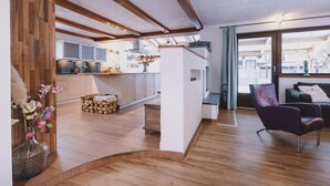 A modern kitchen with wooden beams, a dining area with a sofa and a chair, and a large window with a view. - Appartements Enzian by we rent (Rauris)