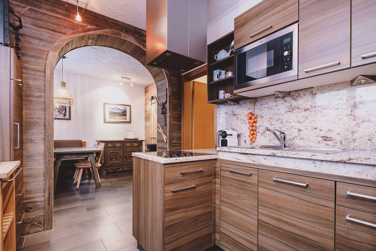A modern kitchen with wooden cabinets, a built-in microwave, and a marble countertop.