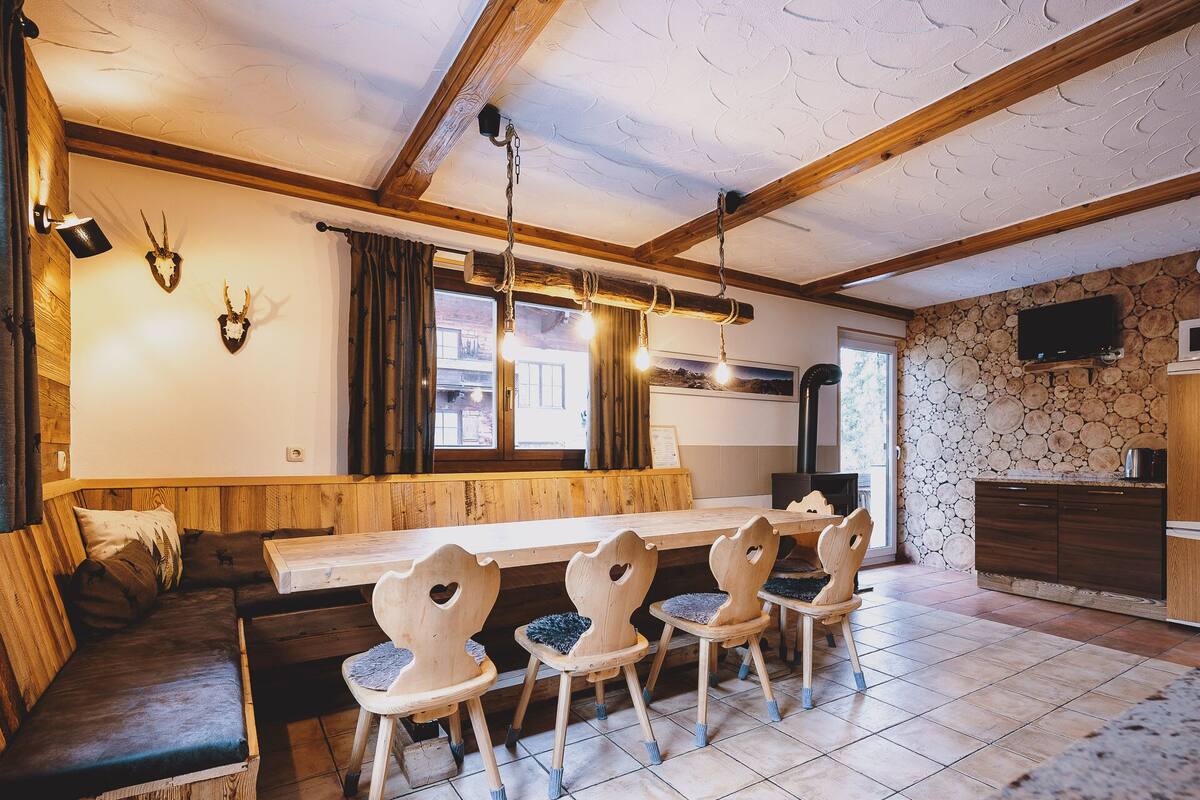 A cozy dining area with a wooden table and chairs, a bench, and a stone wall with a fireplace.