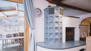 A cozy interior with a fireplace, a clock on the wall, and a view of the outdoors through a glass door. - Appartements Enzian by we rent (Rauris)