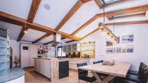 A modern kitchen with wooden beams, a central island, and a dining area with a table and chairs. - Appartements Enzian by we rent (Rauris)