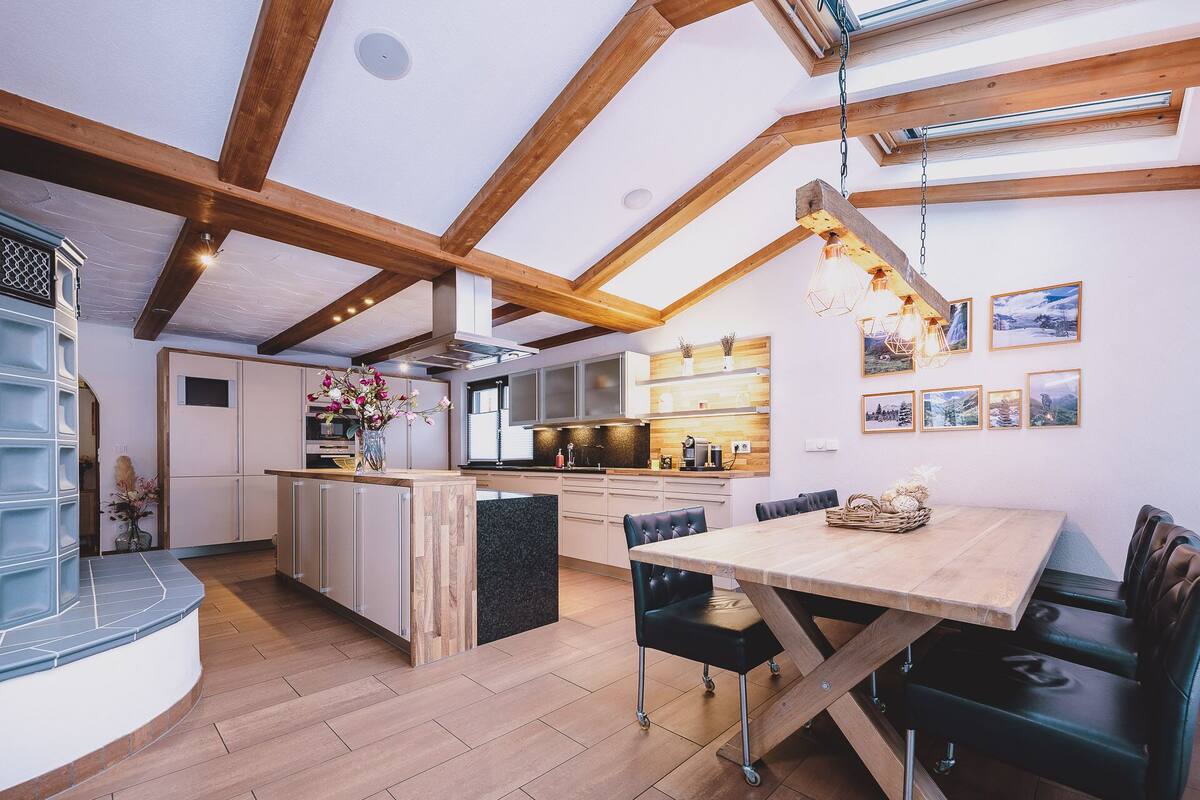 A modern kitchen with wooden beams, a central island, and a dining area with a table and chairs.