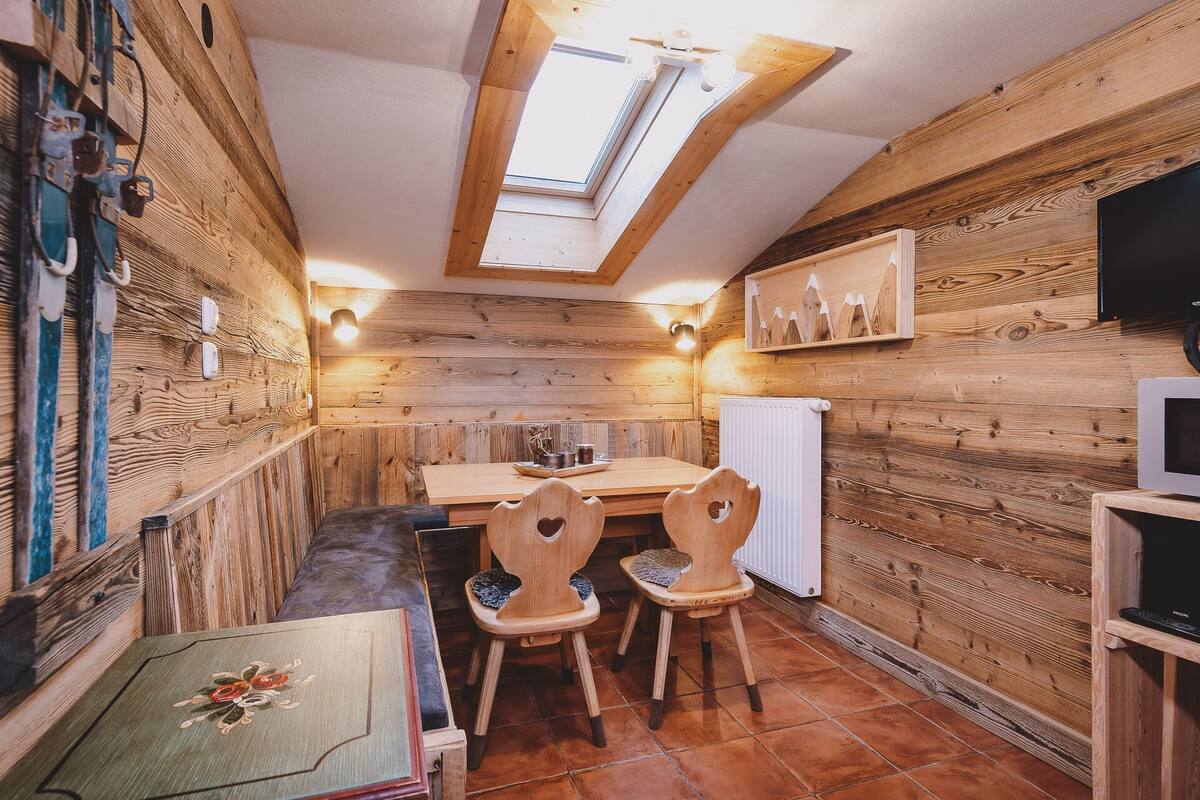 A cozy wooden cabin with a dining area, wooden chairs, a table, and a skylight.