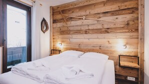 A bedroom with a wooden headboard, a bed with white linens, two bedside tables, and a window with a view of the outside. - Appartements Enzian by we rent (Rauris)