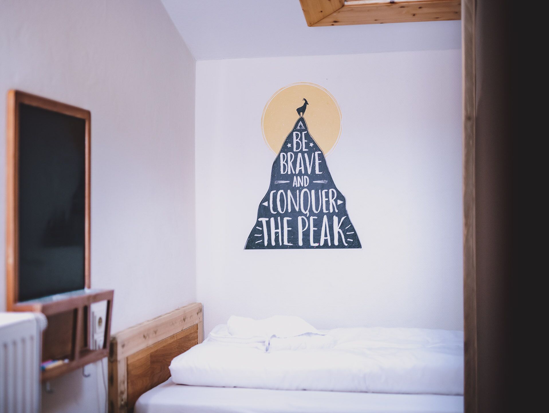 Un dormitorio con una cama, cabecera de madera, pared blanca y un mural con una cita motivacional.