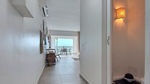 A hallway with a tiled floor, a dining area with chairs and a table, and a wall-mounted light fixture.