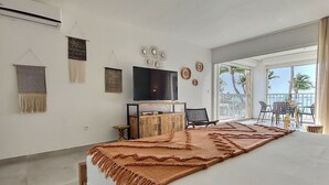 A bedroom with a large bed, a TV, a wooden cabinet, and a balcony with outdoor seating.
