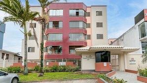 Een meerlaags gebouw met een geel-beige gevel, een hekpoort en een klein overdekt gebied met een bord.