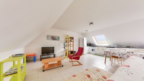 Un amplio loft con techos altos, comedor, cocina y sala de estar con sofá y televisor.